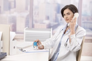 Female doctor sitting at desk in office talking on phone.